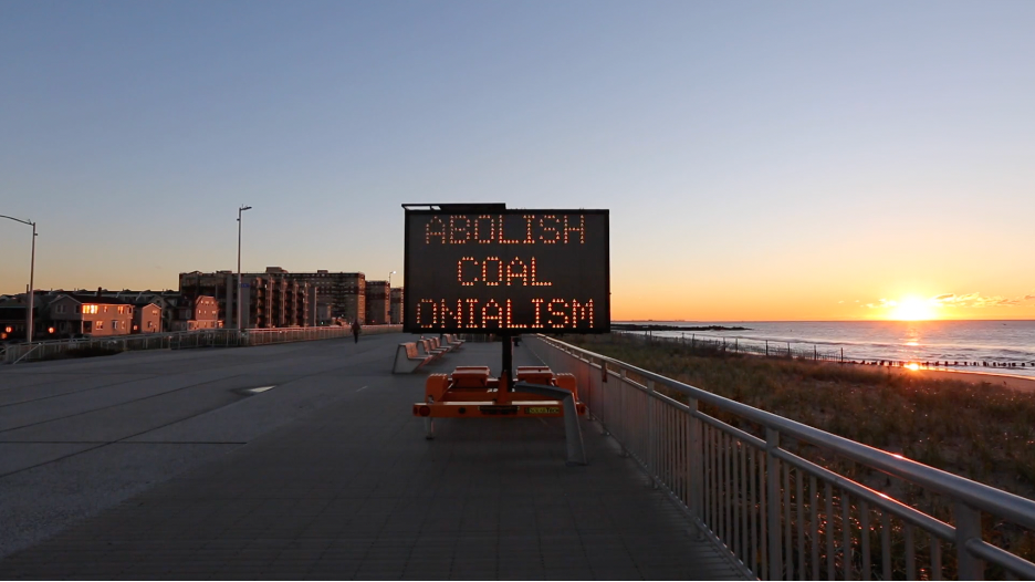 image of lighted road sign read Abolish Coalonialism
